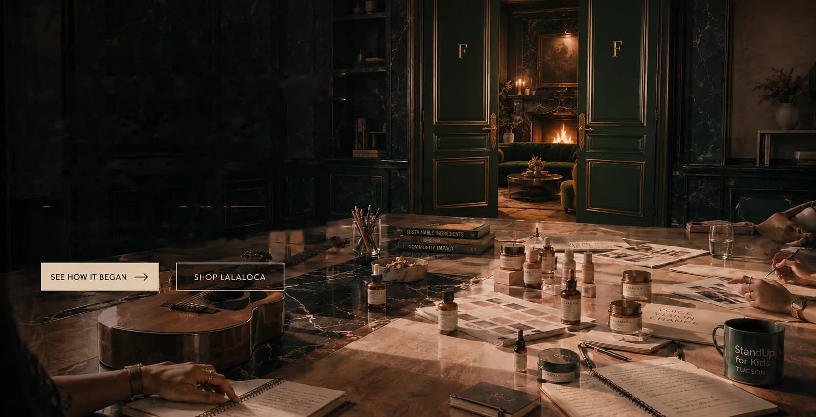 A long table in the FOUNDER house covered in LALALOCA bottles, swatches, notebooks and a guitar, young hands at work along it, the emerald doors open onto the firelit lounge.