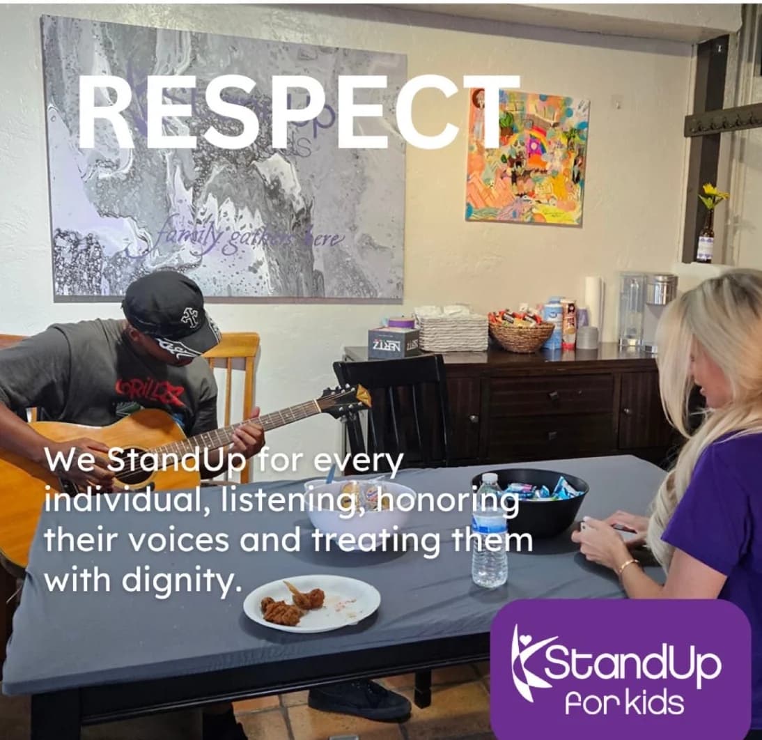 An afternoon at the StandUp for Kids Tucson Outreach Center: a young person playing acoustic guitar at the table while a volunteer listens. The organization's RESPECT graphic reads: We StandUp for every individual, listening, honoring their voices and treating them with dignity.